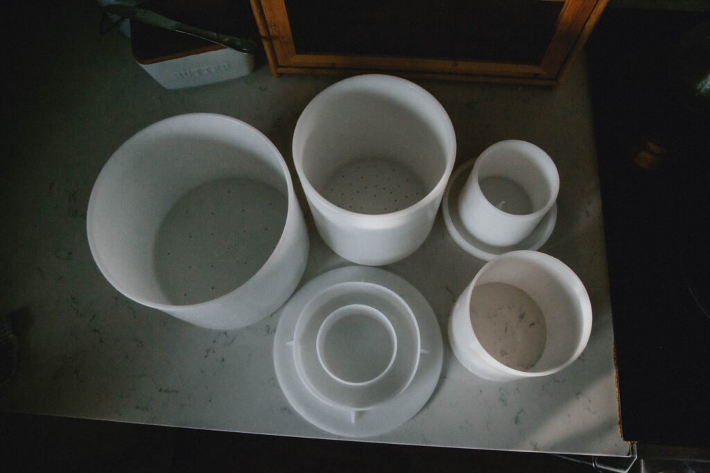 A variety of cheese molds and cheesemaking supplies sits on a countertop.