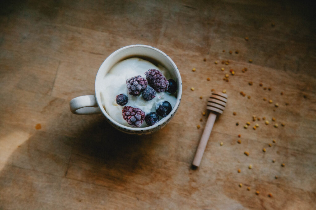 A vintage teacup full of homemade goat milk yogurt and berries sits on a wooden countertop.