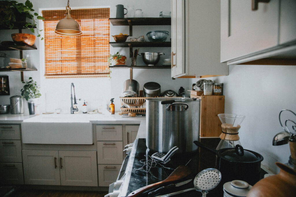 A counter full of cheesemaking supplies, including a large pot, sits in a homestead kitchen.