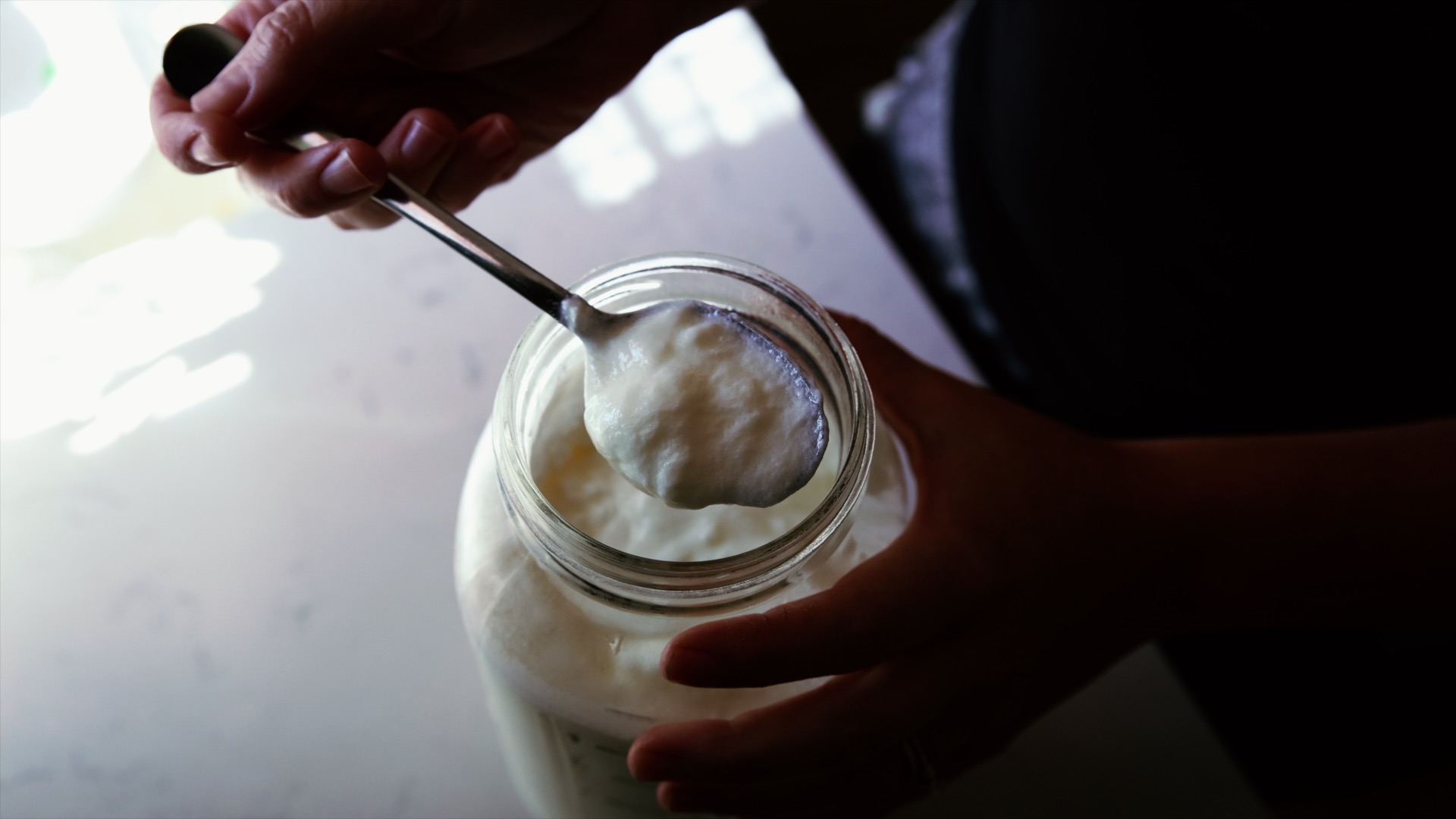 Thick and creamy goat milk yogurt sits in a spoon atop a jar.