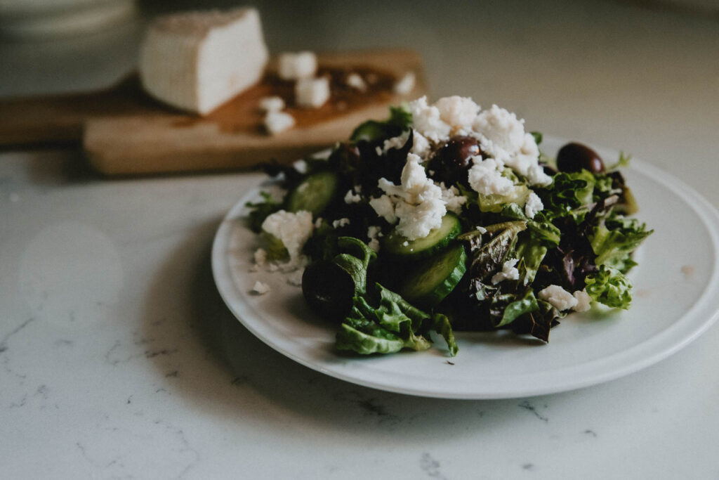 Greek salad topped with goat milk feta cheese sits on a plate on a marble counter.