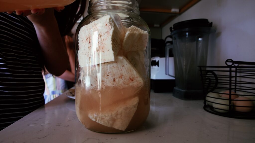 Wedges of feta cheese and salt brine fill a gallon mason jar.
