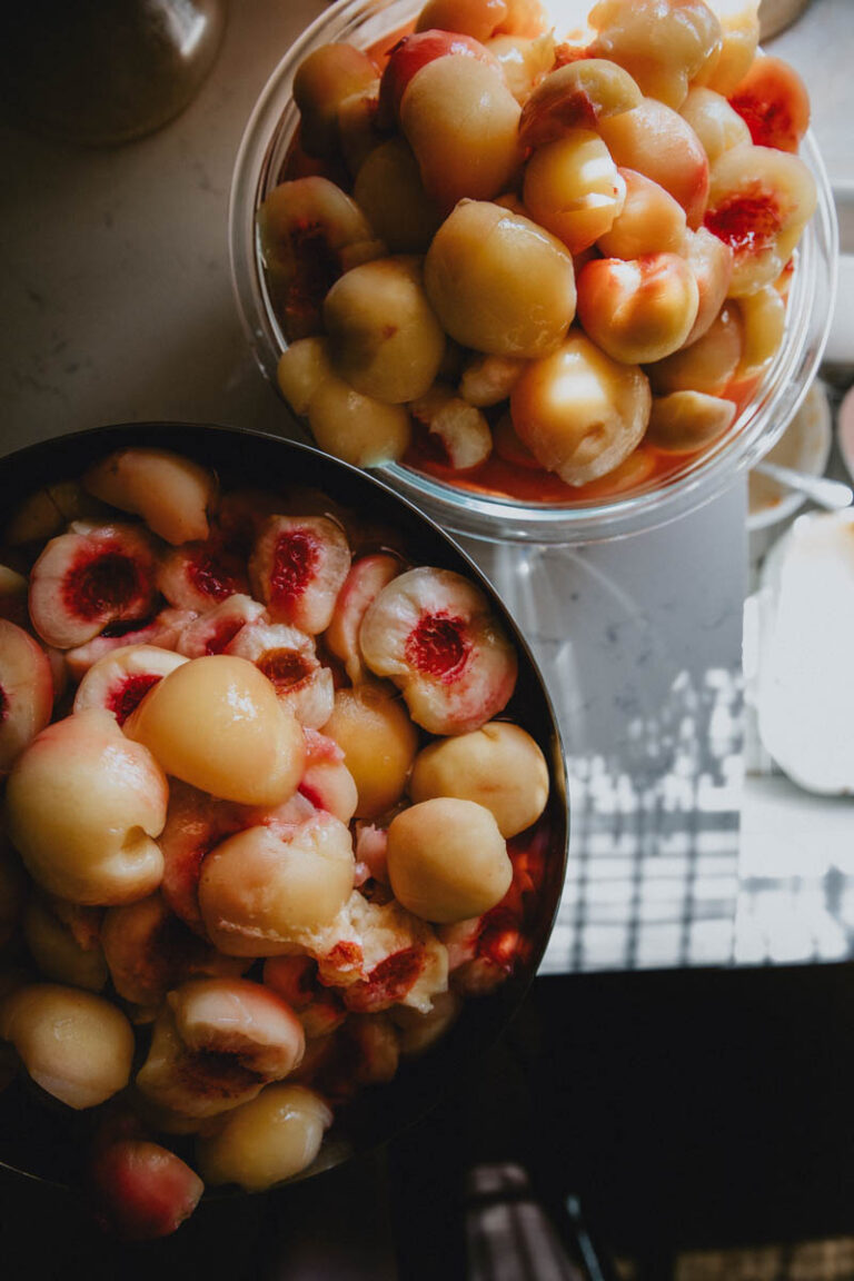 A bowl full of fresh pitted peaches sits on a sunny counter.