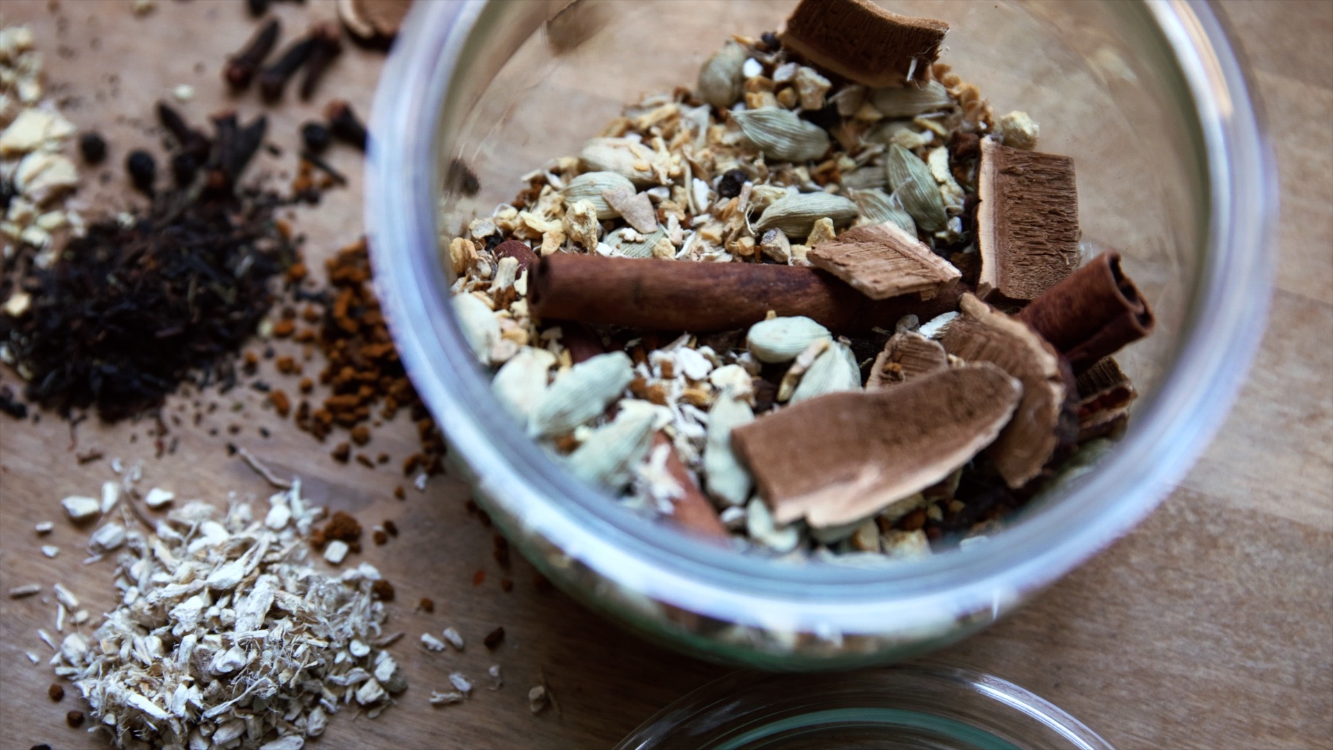 A glass jar full of loose leaf chai and mushrooms sits on a wooden counter.