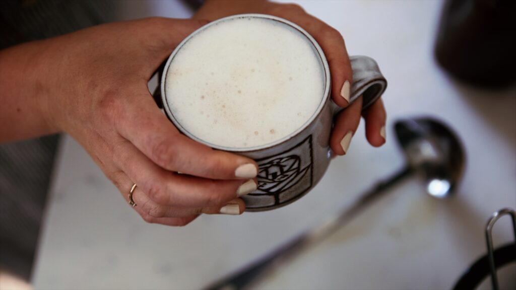 A woman holds a mug of frothy mushroom chai.