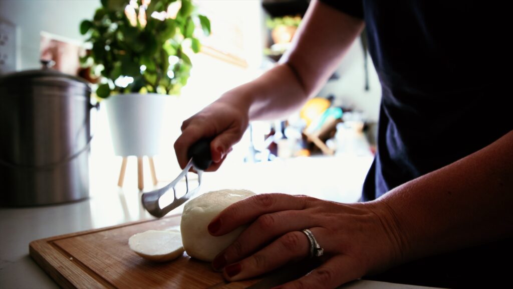 A woman slices a ball of fresh goat milk mozzarella on a cutting board.
