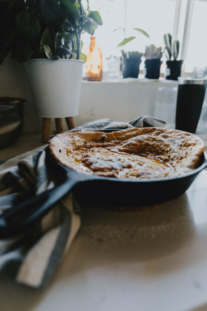 A dutch baby sits on the counter in a frying pan, fresh from the oven.