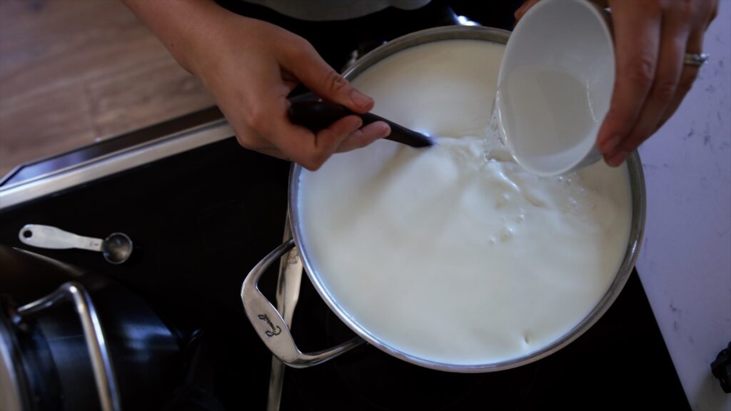 A woman stirs in citric acid to a pot of milk to make goat milk mozzarella.