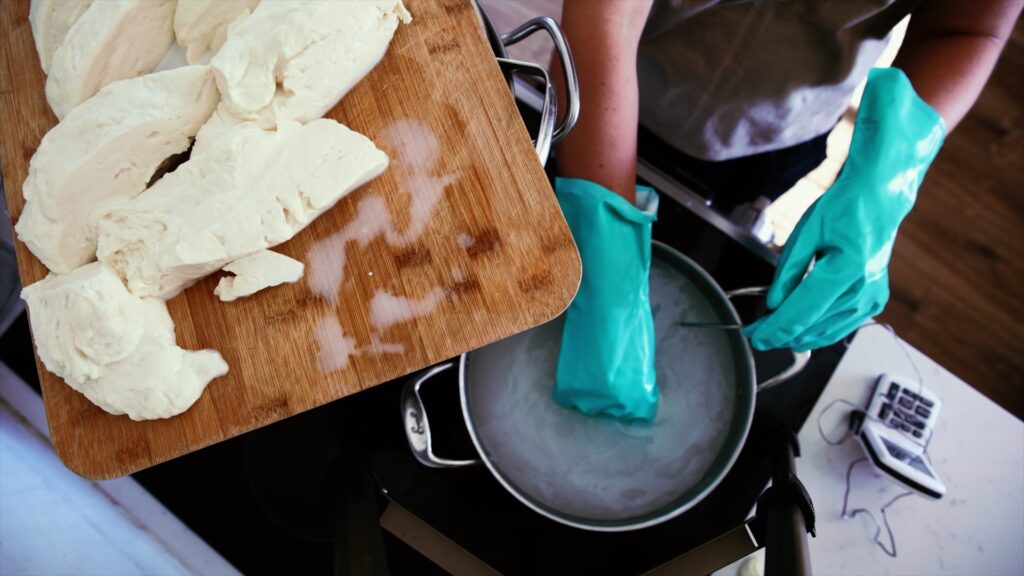 A woman heats mozzarella curds to stretch them into goat milk mozzarella.