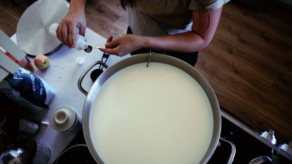 A woman adds rennet to a pot of warm milk to make goat milk mozzarella.