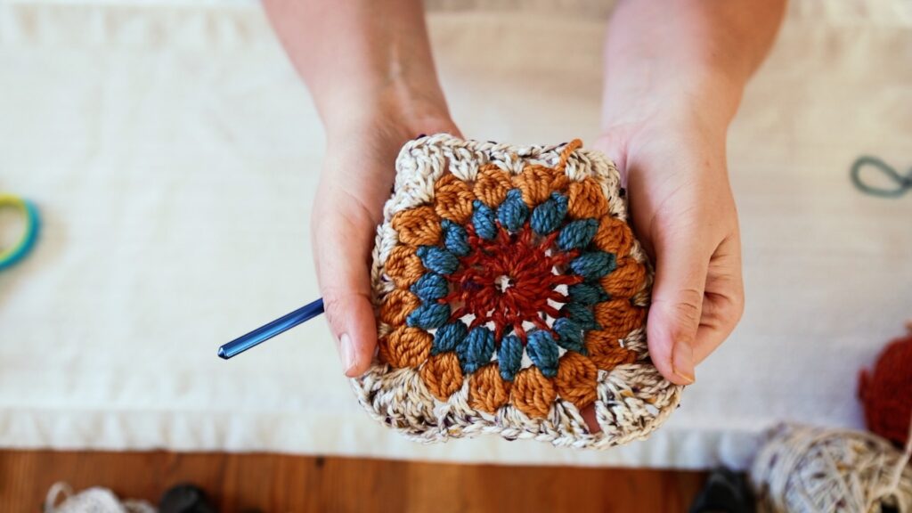 A woman holds a finished sunburst granny square in her hands.