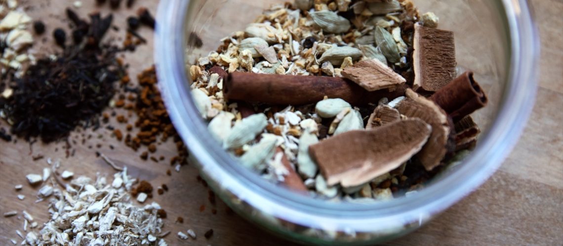 A glass jar full of loose leaf chai and mushrooms sits on a wooden counter.